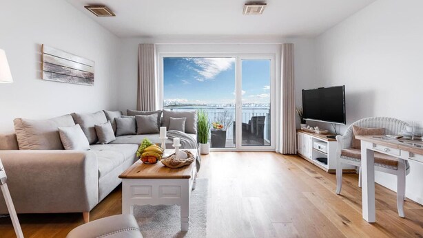 Una sala de estar moderna con un sofá, una mesa de centro, un televisor y un balcón con vista a la ciudad.