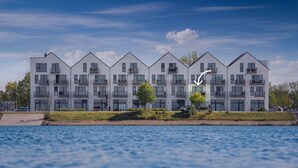 Un edificio residencial moderno de varios pisos con balcones, situado cerca de una masa de agua.