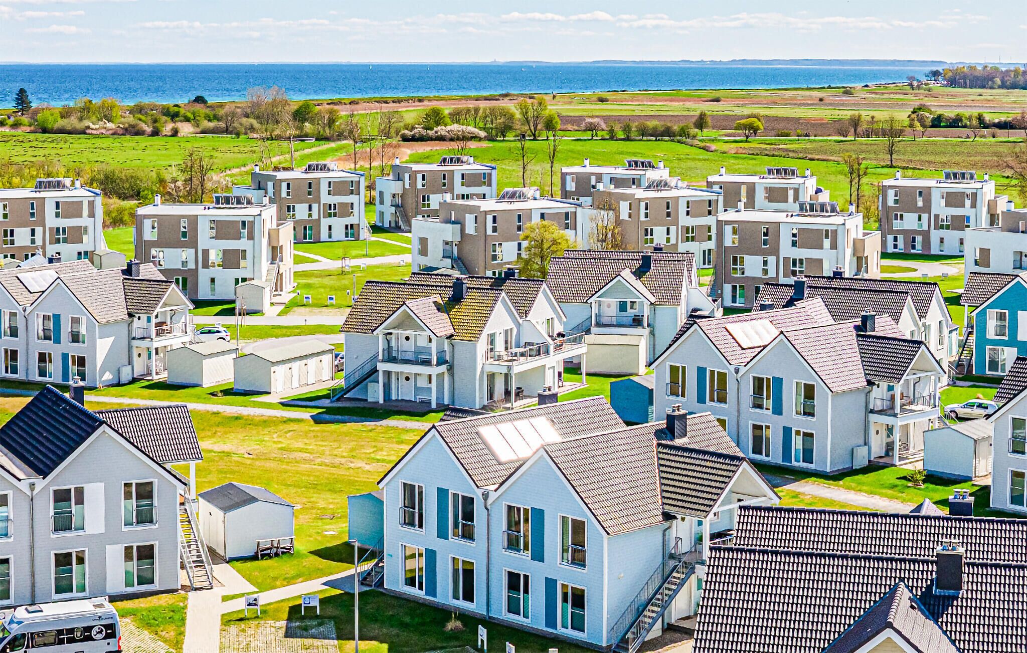 A residential area with multiple two-story houses, some with attached garages, and a view of the sea in the background.
