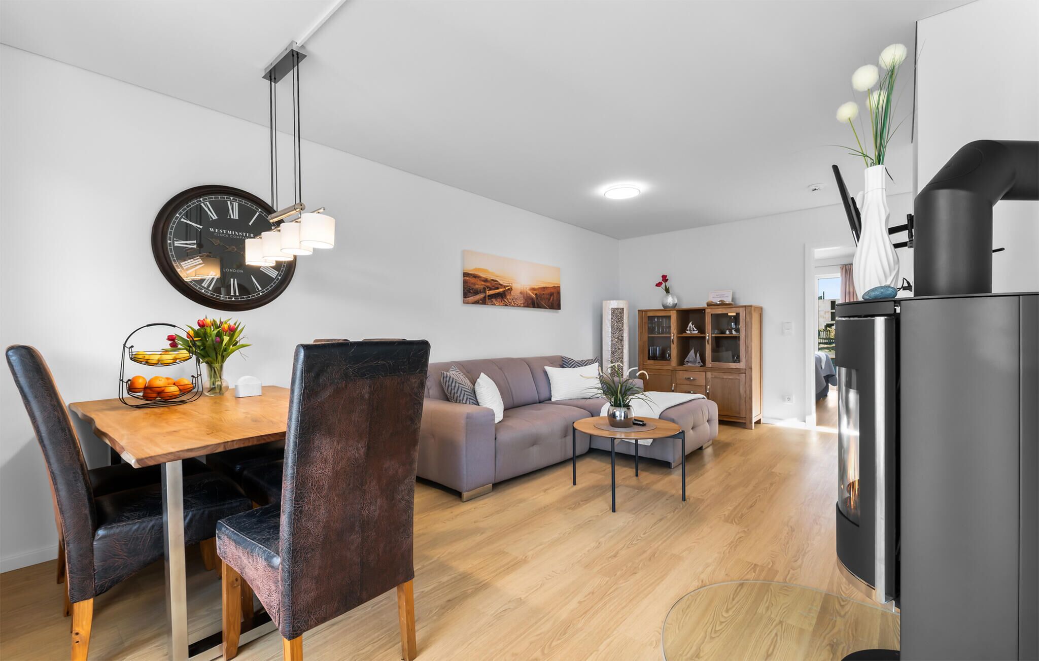 A modern living room with a dining area, a sofa, a coffee table, and a clock on the wall.