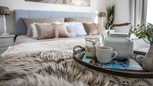Et hyggeligt soveværelse med seng, et natbord med lampe og et bakke med tekande, kopper og en plante.