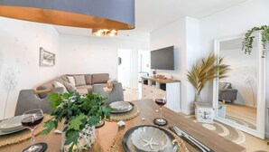 En moderne stue med sofa, spisebord dækket med tallerkener, glas og en plante.