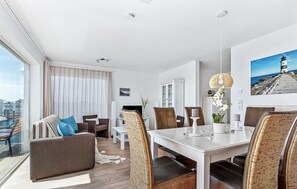 A modern hotel room with a balcony, a dining area, and a view of the cityscape.