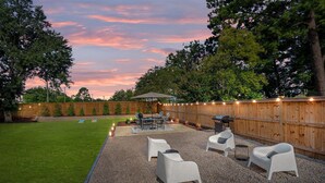 A backyard with a wooden fence, a patio with chairs and a table, and a grassy lawn. - 1 Mile to DT, King Bed, Fenced Yard, Fire Pit, Pet Friendly (Raleigh)