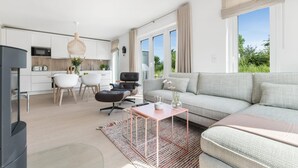 Ett modernt vardagsrum med kök, matplats och ett stort fönster som ger utsikt över grönområden.