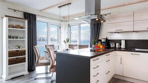 Ett modernt kök med en central köksö, vita köksskåp och utsikt över havet.