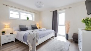 Ett modernt sovrum med en säng, sängbord, ett litet bord, en tv och ett fönster med gardiner.