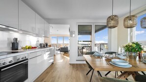 A modern kitchen with white cabinets, a Bosch oven, and a dining area with a wooden table and chairs. - Stunning apartment in Olpenitz (Olpenitz)