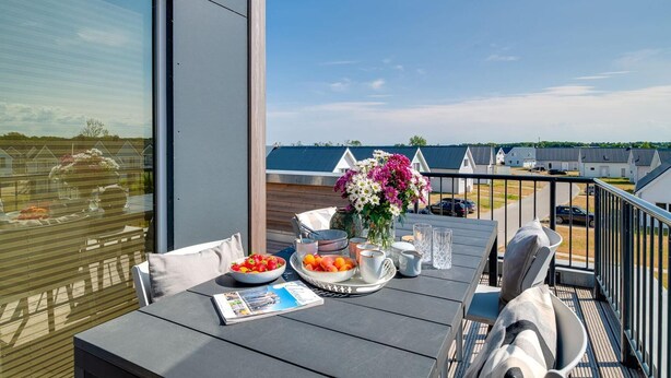 A balcony with a table set for dining, a vase with flowers, and a view of a residential area. - Stunning apartment in Olpenitz (Olpenitz)