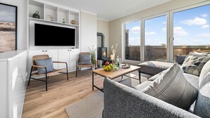 A modern living room with a flat-screen TV, wicker chairs, a sofa, a wooden coffee table with fruit, and a fireplace. - Stunning apartment in Olpenitz (Olpenitz)