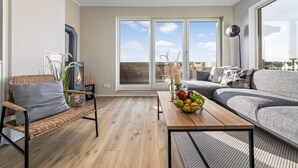 A modern living room with a sofa, a wicker chair, a wooden coffee table with fruit, and a large window with a view. - Stunning apartment in Olpenitz (Olpenitz)