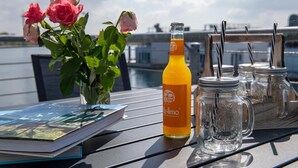 Uma mesa com um livro, um suco de laranja, um vaso com rosas cor-de-rosa e potes de vidro com canudos.