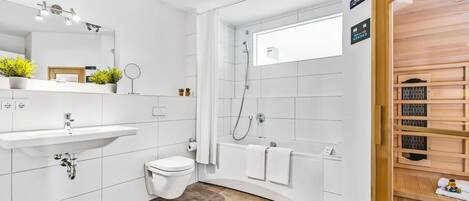 A modern bathroom with a white sink, toilet, and shower. There are plants on the sink, a mirror, and a towel rack.