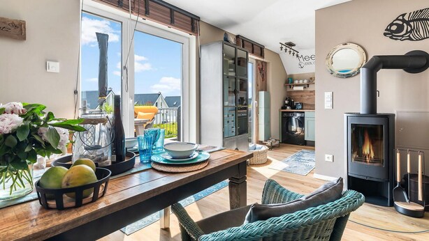 A modern kitchen with a large window, a dining area with a wooden table, and a built-in wood stove. - Gorgeous apartment in Olpenitz (Olpenitz)