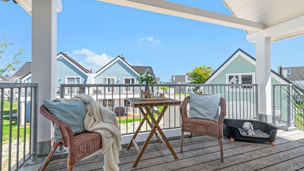 Un espace extérieur abrité, aménagé avec des chaises en osier, une petite table ornée d’un vase et un panier pour chien.