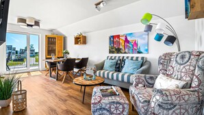 Un salon moderne comprenant un coin repas, une grande fenêtre offrant une vue panoramique et un tableau coloré représentant un paysage urbain.