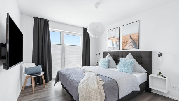 Une chambre à coucher moderne avec un lit, une télévision, un fauteuil et des œuvres d’art accrochées au mur.