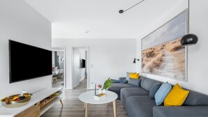 Un salon moderne doté d’un grand téléviseur à écran plat, d’un canapé gris agrémenté de coussins jaunes, d’une table basse blanche et d’un grand tableau abstrait accroché au mur.