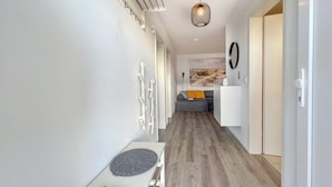 Un couloir moderne avec un plancher en bois, des murs blancs et un canapé gris en arrière-plan.