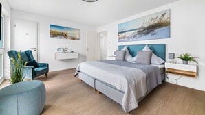 Une chambre à coucher moderne avec un grand lit, un fauteuil bleu, une table d’appoint avec une plante et des œuvres d’art accrochées aux murs.