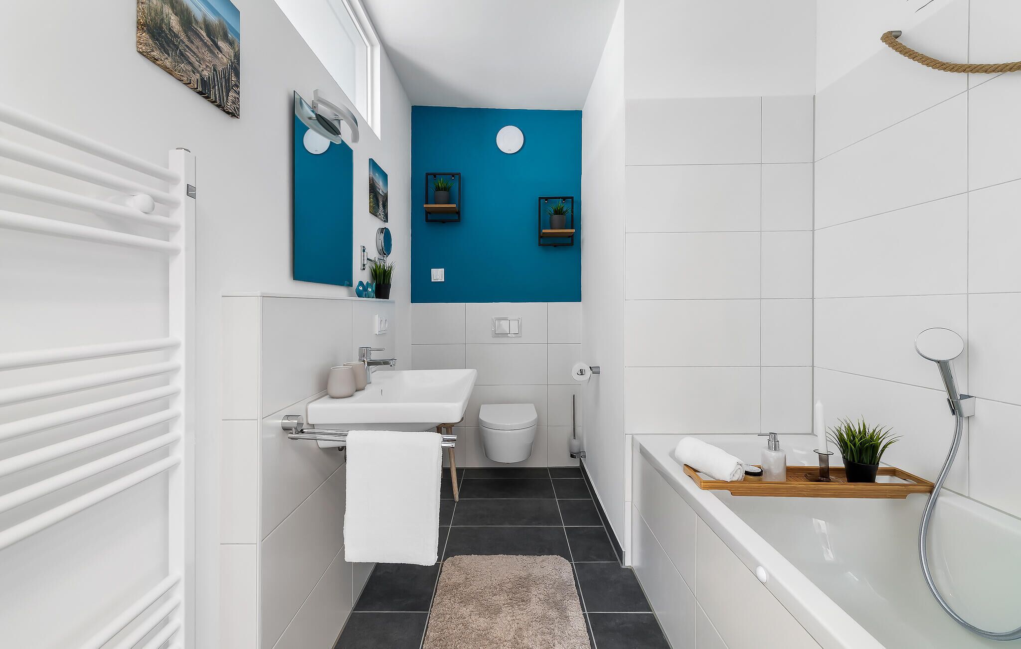 Un baño moderno con lavamanos, inodoro y bañera blancos, una pared azul decorativa y un pequeño estante con una planta.