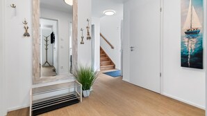 Un couloir avec un plancher en bois, un miroir, un escalier et un tableau représentant un voilier.