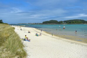 En strand med solbadere og badende, både i vandet og et græsområde til venstre.