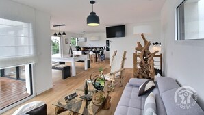 A modern living room with a glass coffee table, a sofa, and a dining area with a kitchen in the background. - Le Menhir - PLEUMEUR BODOU (PLEUMEUR BODOU)