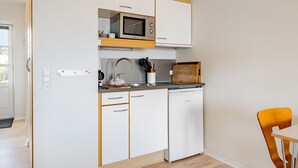Une cuisine de taille réduite avec des meubles blancs, un four à micro-ondes, un évier et une planche à découper en bois.