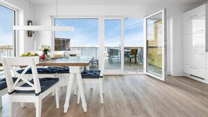 A modern kitchen with white cabinets, a wooden dining table, and a view of the deck.