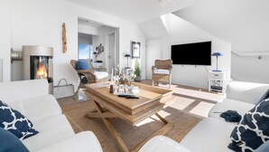 A modern living room with a fireplace, two wicker chairs, a wooden coffee table, and a flat-screen TV mounted on the wall.