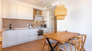 Una cocina moderna con armarios blancos, encimera de madera, horno empotrado y comedor con mesa y sillas de madera.