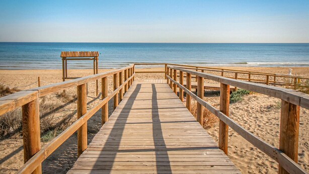 Un muelle de madera que conduce a una playa, con un banco y vista despejada al océano.
