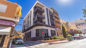 Un edificio moderno de varios pisos con balcones, una tienda visible en la planta baja y un cielo despejado.