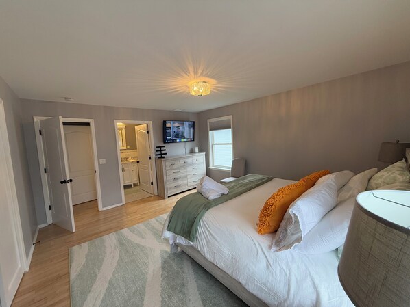 A bedroom with a bed, a dresser, a television, and a bathroom visible through an open door.