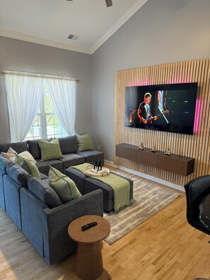 A modern living room with a sectional sofa, a round coffee table, and a flat-screen TV mounted on a wooden panel wall.