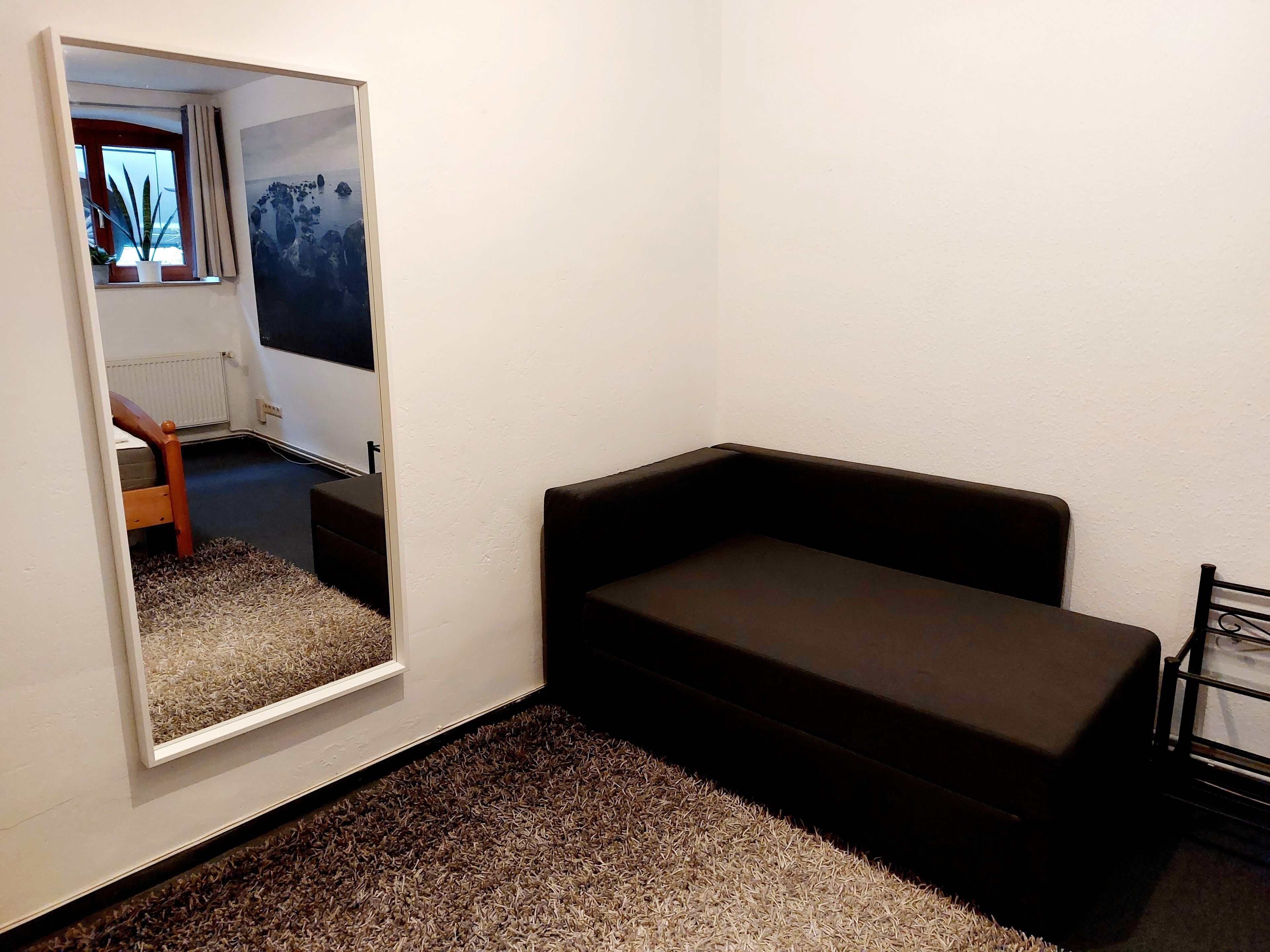 A small room with a dark sofa, a large mirror, and a carpeted floor.