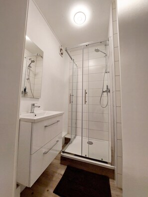 A modern bathroom with a glass-enclosed shower, a white sink, and a mirror. - Central vacation apartment on the lake and near the castle (Schwerin)
