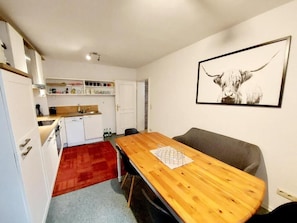 A compact kitchen with white cabinets, a wooden dining table, and a grey sofa.