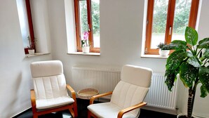 Ein Zimmer mit zwei weißen Sesseln, einem kleinen runden Tisch und einem Blumentopf.