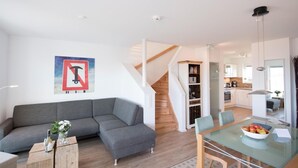 A modern living room with a grey sectional sofa, a glass dining table with chairs, a staircase leading to a kitchen, and a white ceiling with a smoke detector. - Nice home in Olpenitz with sauna (Olpenitz)