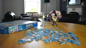 Pöydällä on palapeli, ja sen vieressä on laatikko, jossa lukee: ”1000-osainen Ravensburger-palapeli”, sekä maljakko, jossa on kukkia.