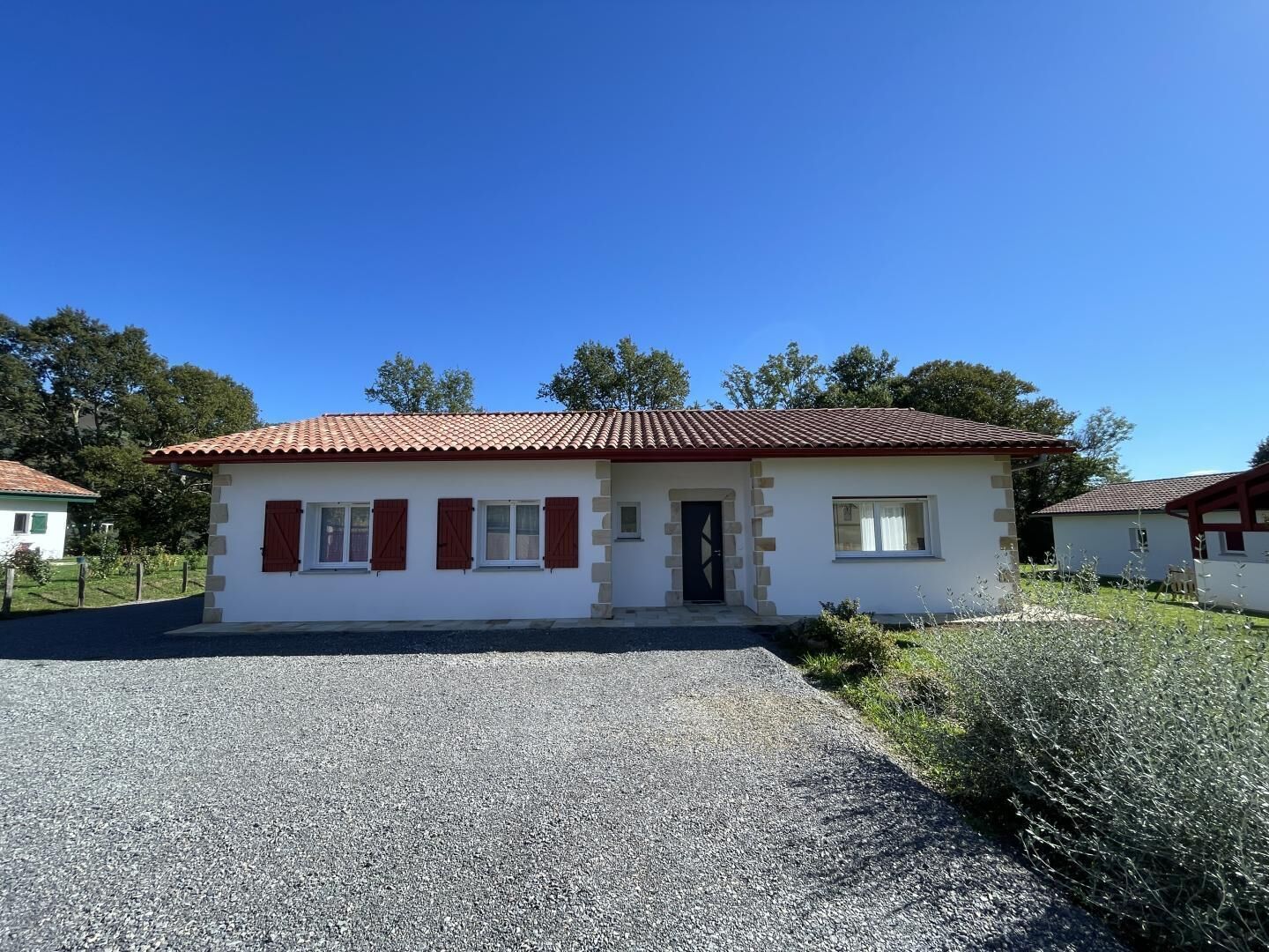 A small, single-story building with a red-tiled roof and white walls, featuring a front door and two windows with shutters.