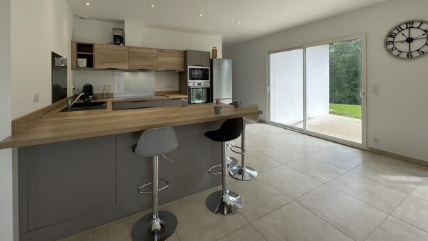 Eine moderne Küche mit Holztischplatte, Edelstahlgeräten und zwei Barhocker.