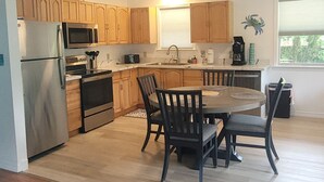A modern kitchen with wooden cabinets, stainless steel appliances, and a dining area with a round table and chairs.