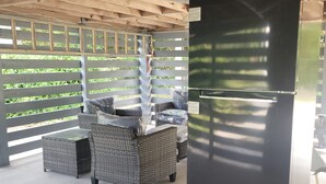 A covered outdoor area with wicker furniture and a black refrigerator.