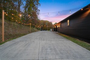 Un chemin en béton mène à un bâtiment, et des guirlandes lumineuses sont suspendues au-dessus.