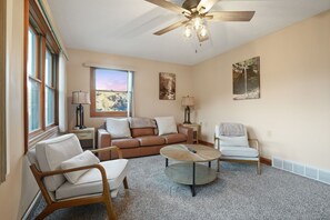 A living room with a brown leather sofa, two white armchairs, a round coffee table, and a ceiling fan.