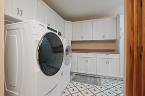 A laundry room with a front-loading Whirlpool washer and dryer, white cabinetry, and patterned floor tiles.