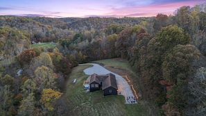 A house with a paved driveway, surrounded by a forested area.